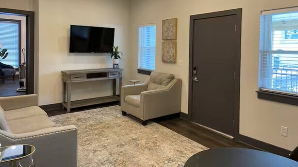 Un salon comprenant un téléviseur, un canapé, un fauteuil, une console et une porte.