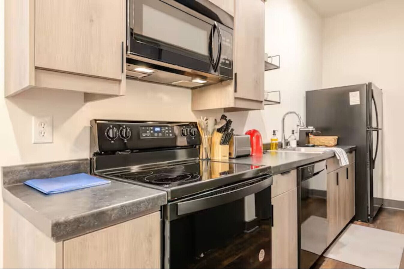 Een moderne keuken met een roestvrijstalen fornuis, een magnetron en een koelkast, houten kastjes en een granieten aanrecht.