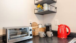 Una kitchenette equipada con tostadora, cafetera, tazas y un hervidor rojo.