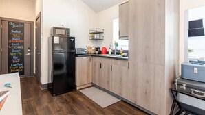 Una cocina moderna con un refrigerador negro, armarios de madera, una encimera con varios objetos y un menú en pizarra que enumera servicios como desayuno y tienda de vinos.