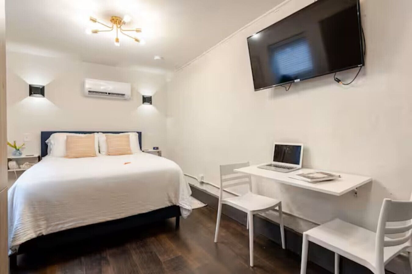 Une chambre d’hôtel avec un lit, un bureau avec un ordinateur portable, une télévision et deux chaises.