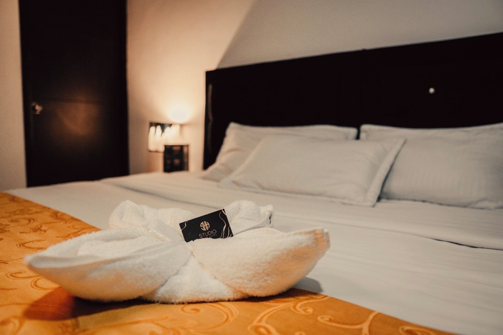 Ein ordentlich bezogenes Bett mit weißen Leinen und Kissen, ein gefaltetes Handtuch auf dem Bett und eine kleine Karte darauf.