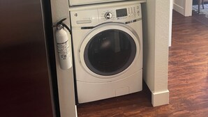 A compact laundry area with a top-loading washer and a front-loading dryer, a fire extinguisher, and a stainless steel refrigerator.