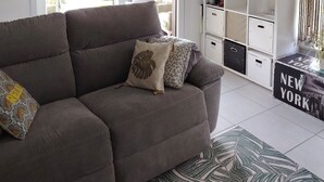 Una sala de estar con sofá, candelabro, ventana con persianas, lámpara y unidades de almacenamiento.