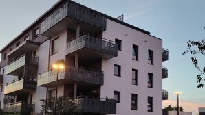 Un edificio residencial de varios pisos con balcones, una entrada protegida por un portón y vista a la calle.