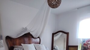 Un dormitorio con cama a dosel, cabecera de madera, mesita de noche, espejo y adorno floral.