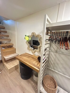 A bedroom with a wooden desk, a mirror, a TV, a wardrobe with hanging items, and a staircase. - Ban Tao Tropical Rooftop near central festival waterpark (Phuket)