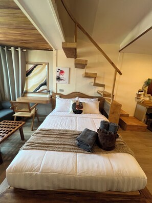A bedroom with a large bed, a wooden staircase, a desk with a chair, and a painting on the wall. - Ban Tao Tropical Rooftop near central festival waterpark (Phuket)