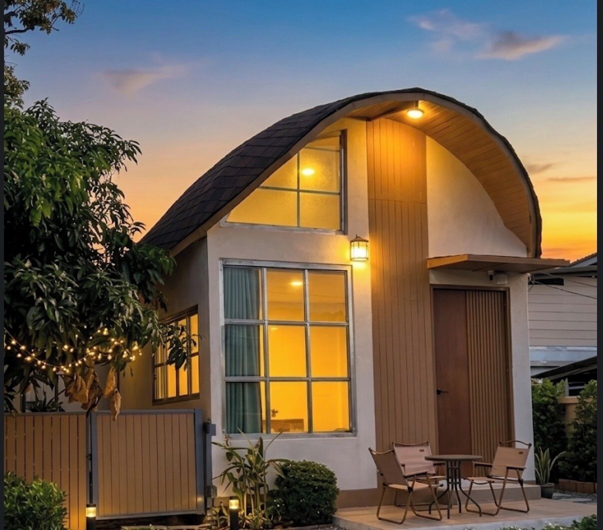 Una casa moderna con techo curvo, grandes ventanales y un pequeño patio con sillas.