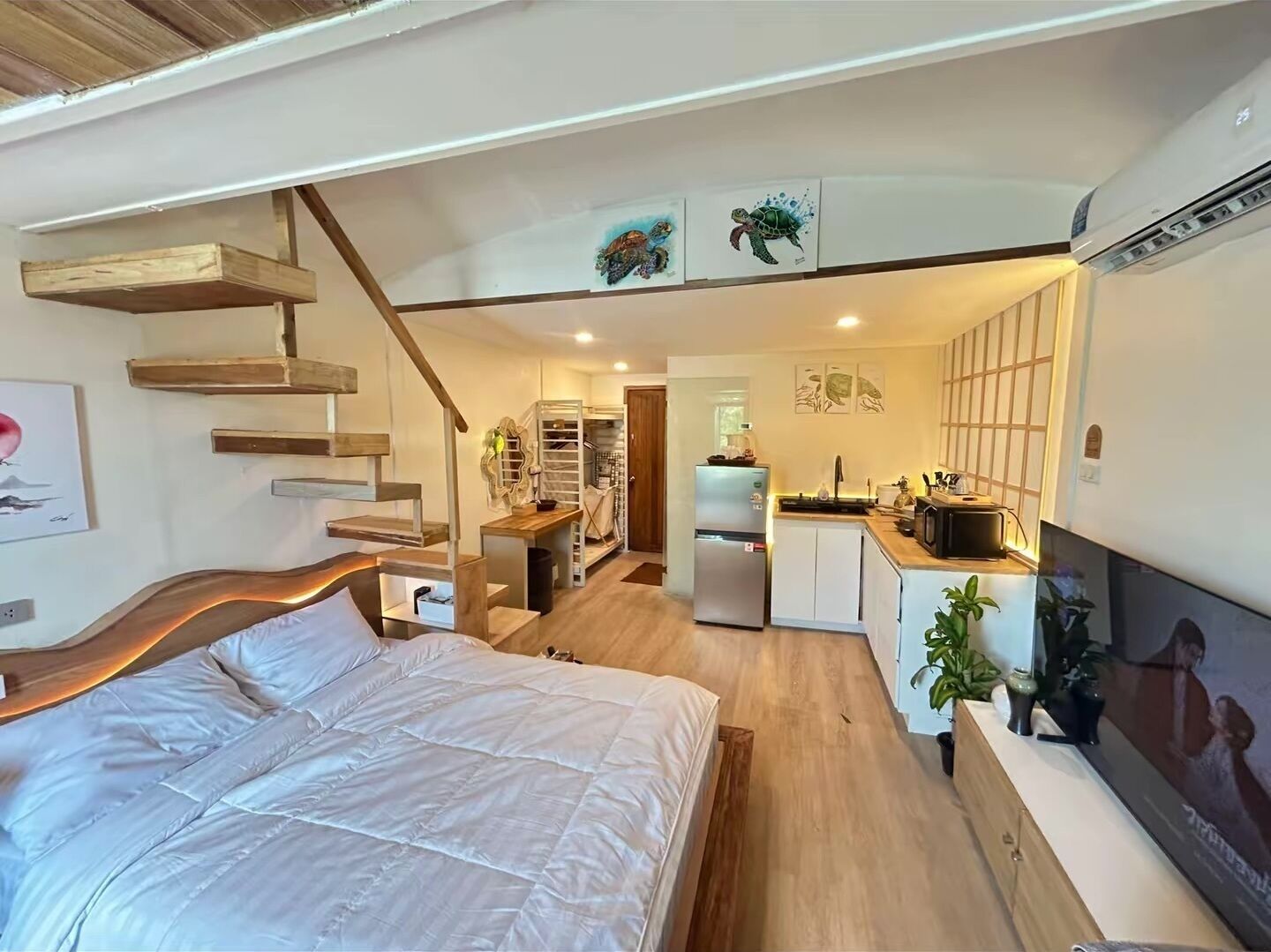 Ett kompakt bostadsutrymme med en säng, ett litet kök och en trappa som leder upp till en övre våning.