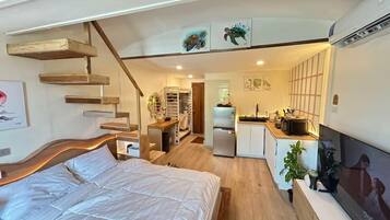 Ett kompakt bostadsutrymme med en säng, ett litet kök och en trappa som leder upp till en övre våning.
