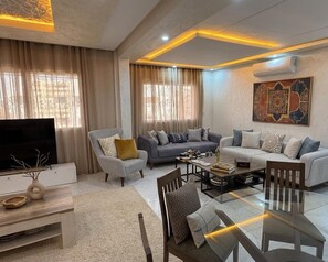 A modern living room with a flat-screen TV, two sofas, a coffee table, and a dining table.