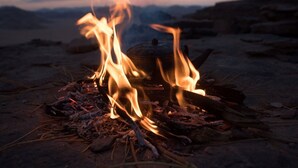 Ein Lagerfeuer mit Holzscheiten und einem Topf auf dem Boden.