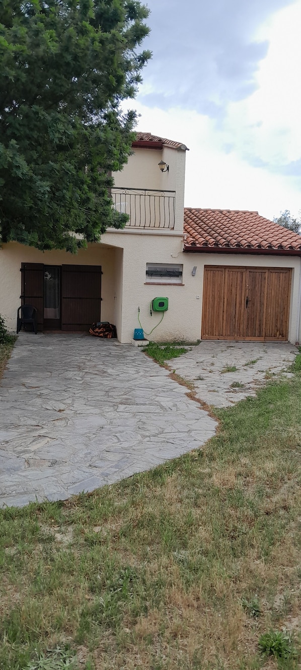 A building with a tiled roof, a stone-paved driveway, and a large tree.