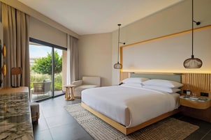Una habitación de hotel moderna con una cama grande, un área de descanso con una silla y una mesa, y vistas a zonas verdes.