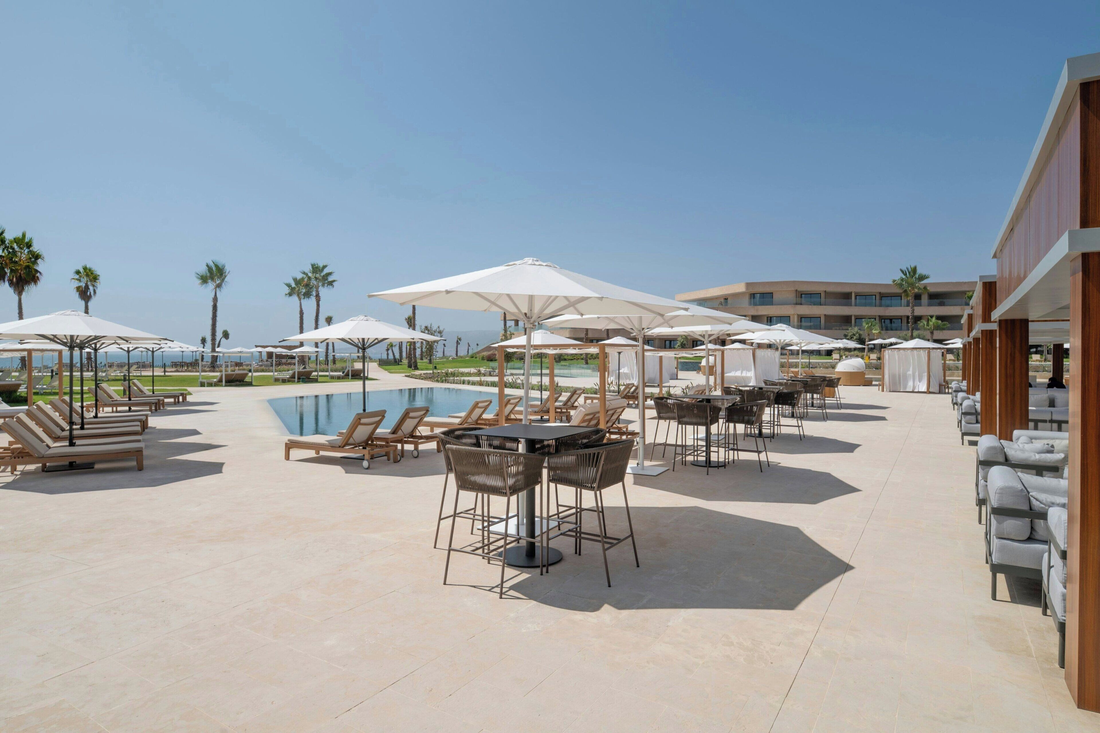 Zona junto a la piscina con tumbonas, sombrillas y mobiliario exterior.