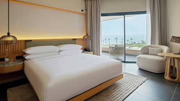 Habitación de hotel con una cama grande, un escritorio con lámpara, una silla y vista a la playa.