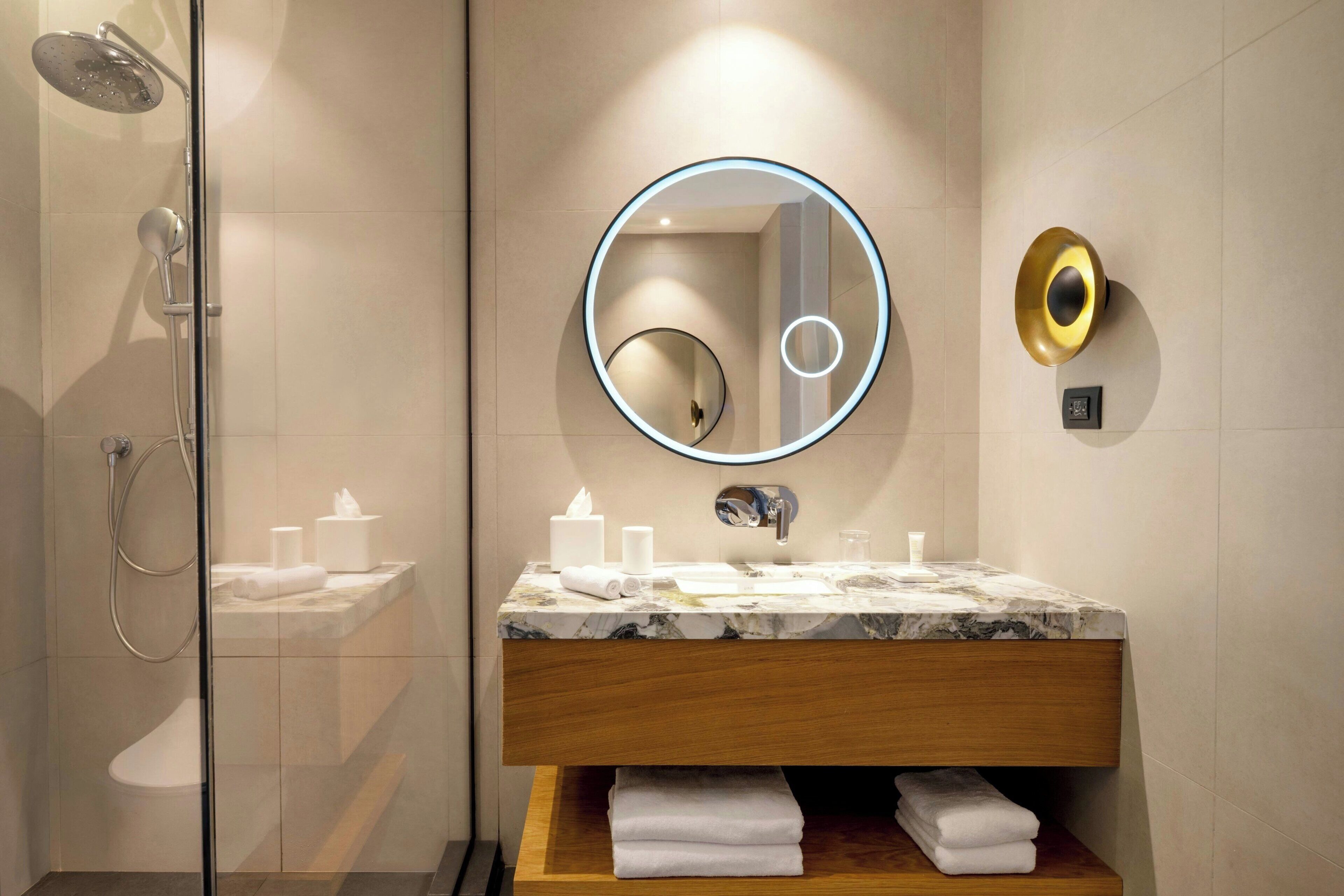 A modern bathroom with a glass shower enclosure, a marble sink, and a wooden vanity.