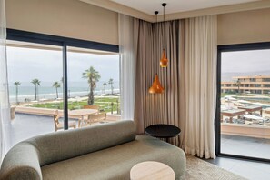 Habitación de hotel moderna con un ventanal que ofrece vistas a la playa y la piscina.