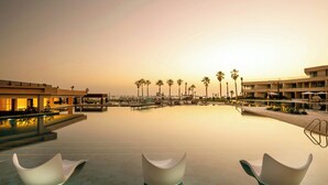 Ein Resort-Pool mit modernen Liegestühlen, Palmen und wolkenlosem Himmel.
