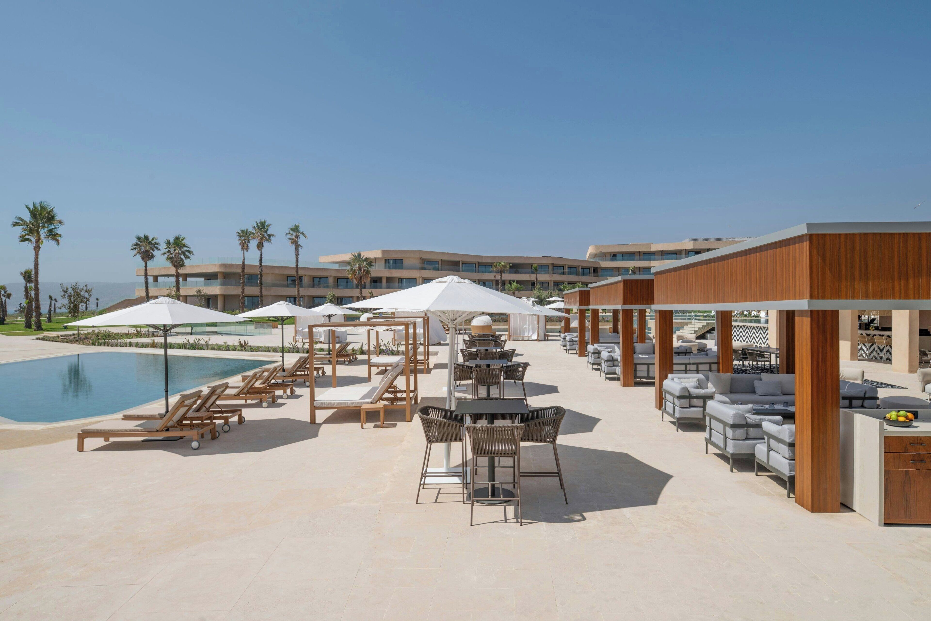 Un área junto a la piscina con sillones de descanso, sombrillas y mobiliario de exterior.