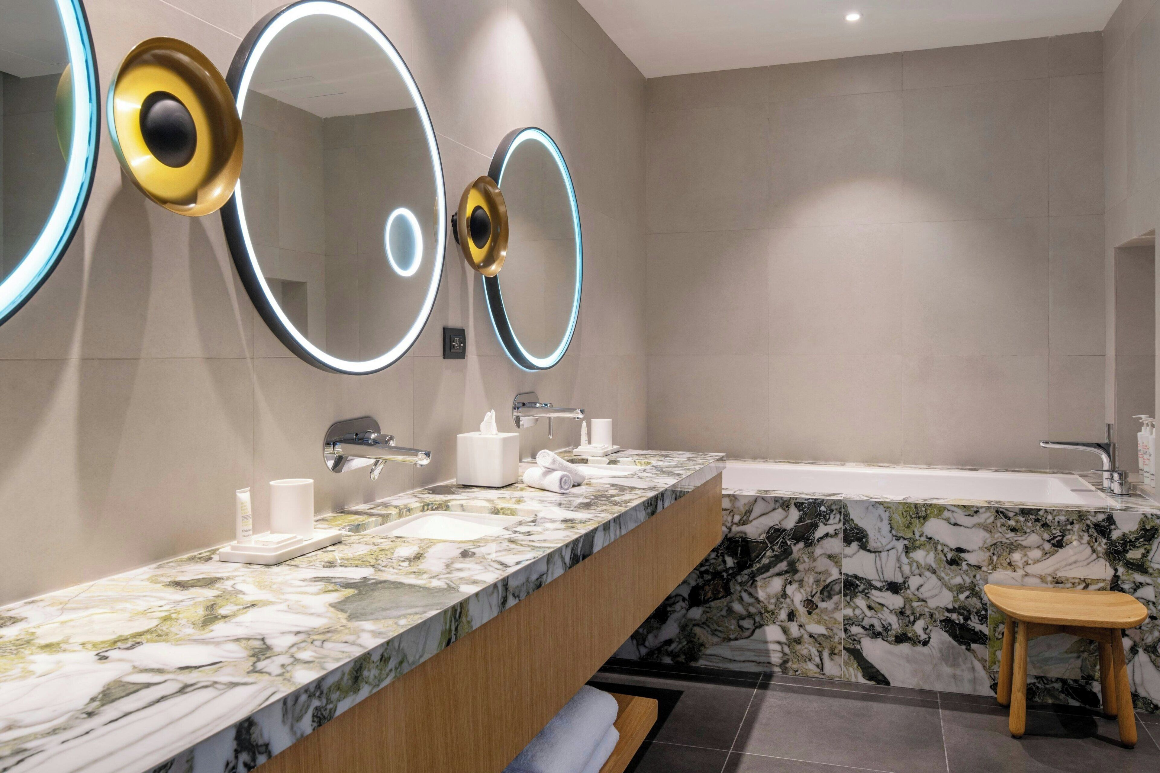 A modern bathroom with a marble vanity, a bathtub, and a wooden stool.