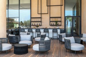 Un espacio exterior moderno con asientos de mimbre y una barra con estantes llenos de botellas.