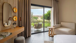 Ein modernes Hotelzimmer mit einer großen Schiebeglasdoor zum Balkon, einem Bett, einer Sitzecke und einem Schminktisch mit Spiegel und Lampen.