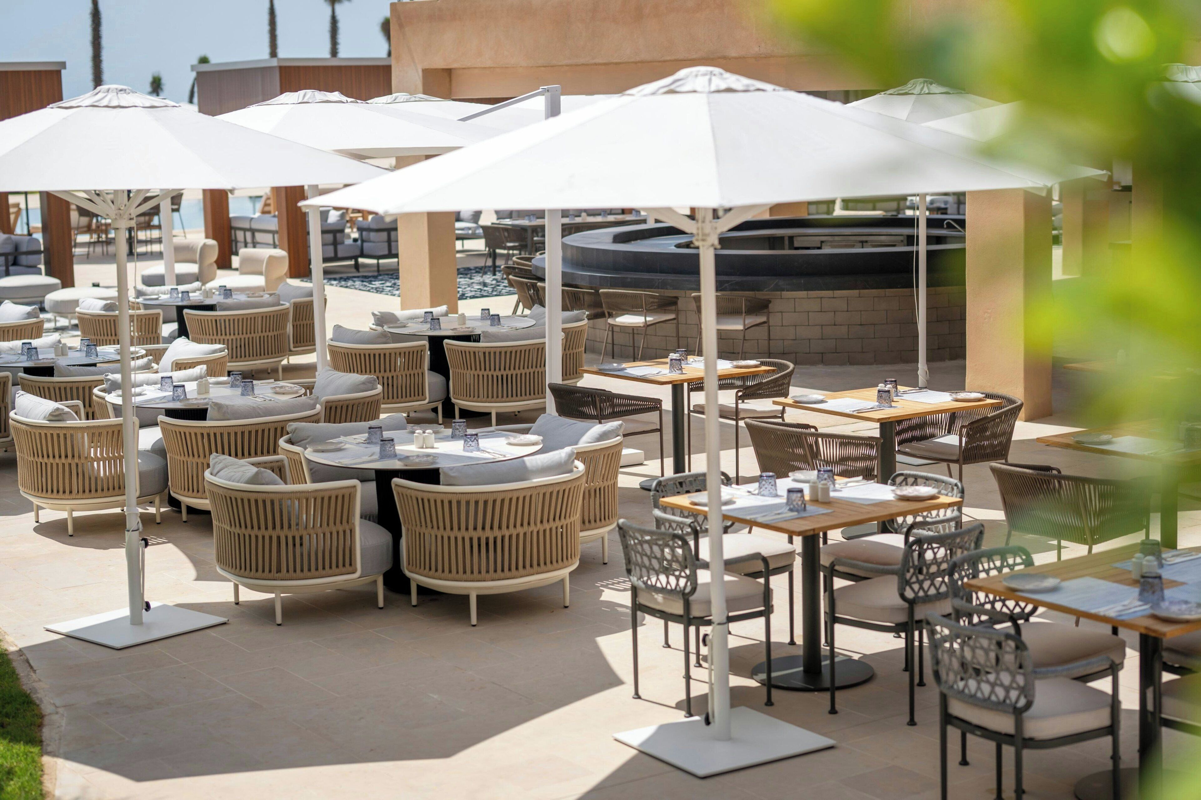 An outdoor patio area with round tables and wicker chairs, some with umbrellas.