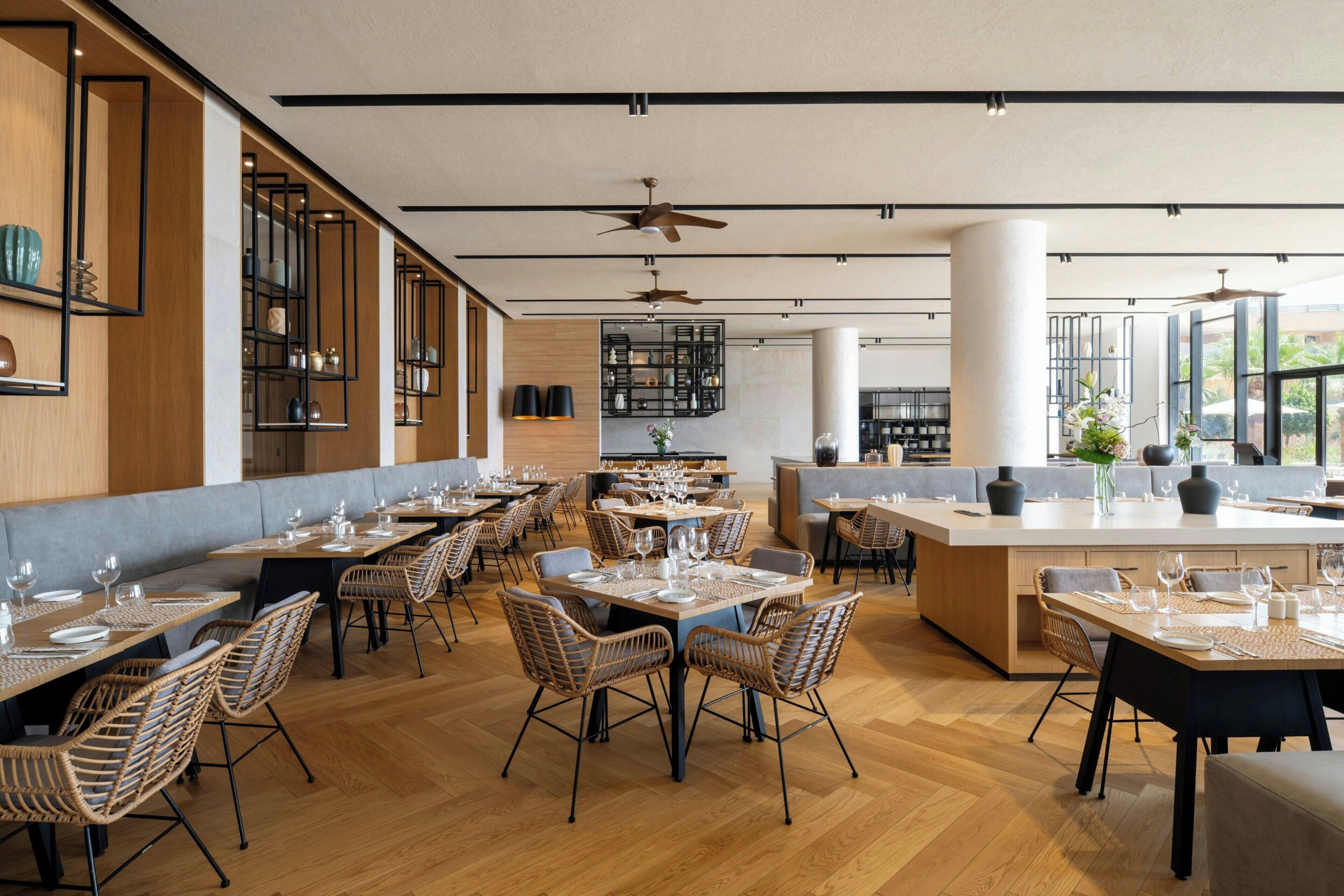 A modern restaurant with wooden flooring, wicker chairs, and a central island with seating.