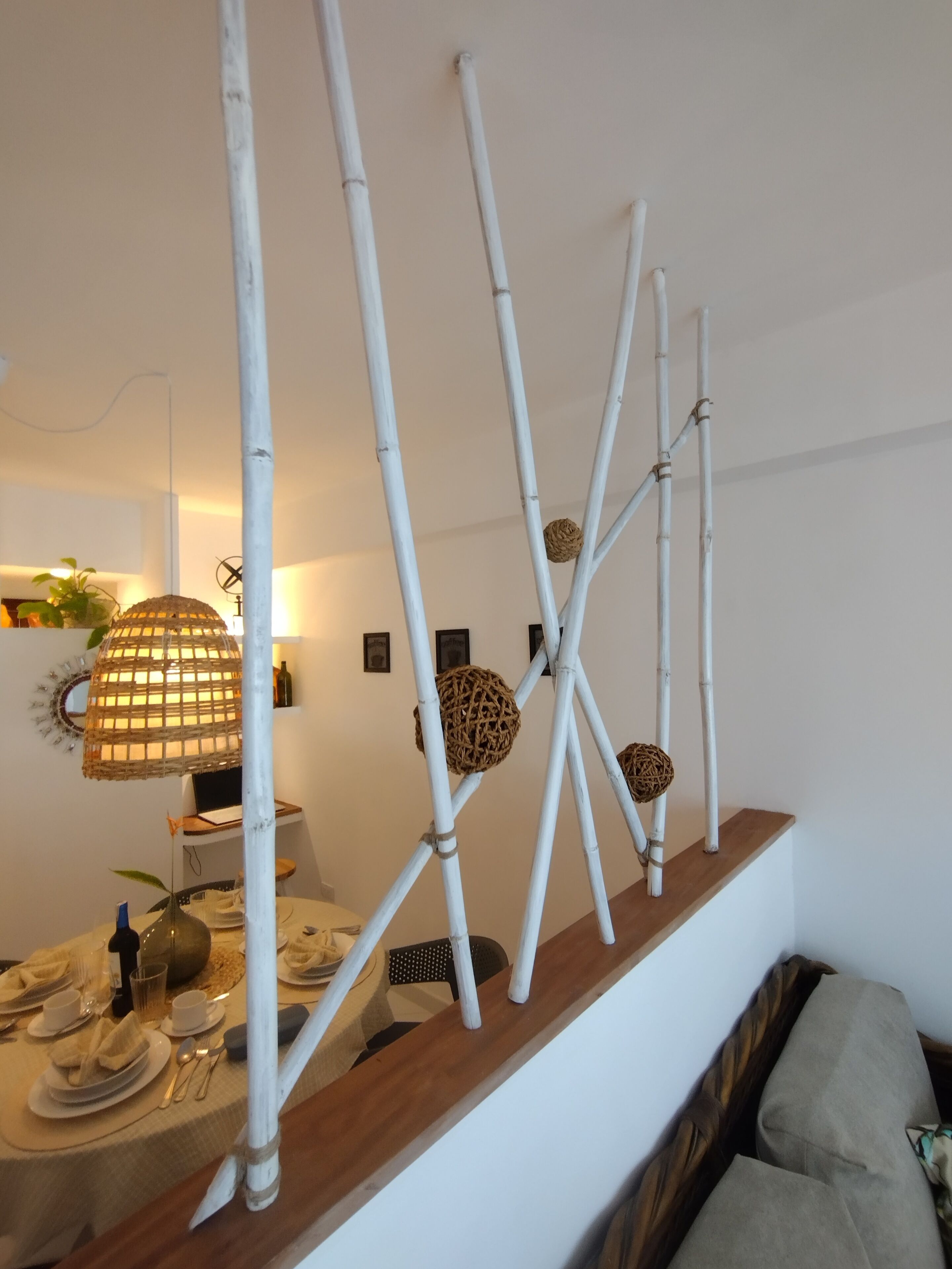 Un comedor con mesa de madera dispuesta para cuatro, listones de bambú blancos y esferas tejidas como decoración.