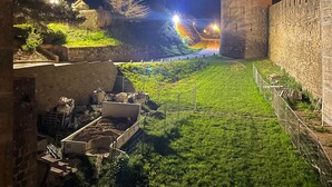Vista nocturna de un castillo histórico con foso, murallas de piedra y una torre.