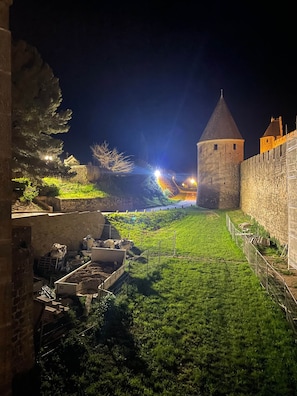 Vista nocturna de un castillo histórico con foso, murallas de piedra y una torre.