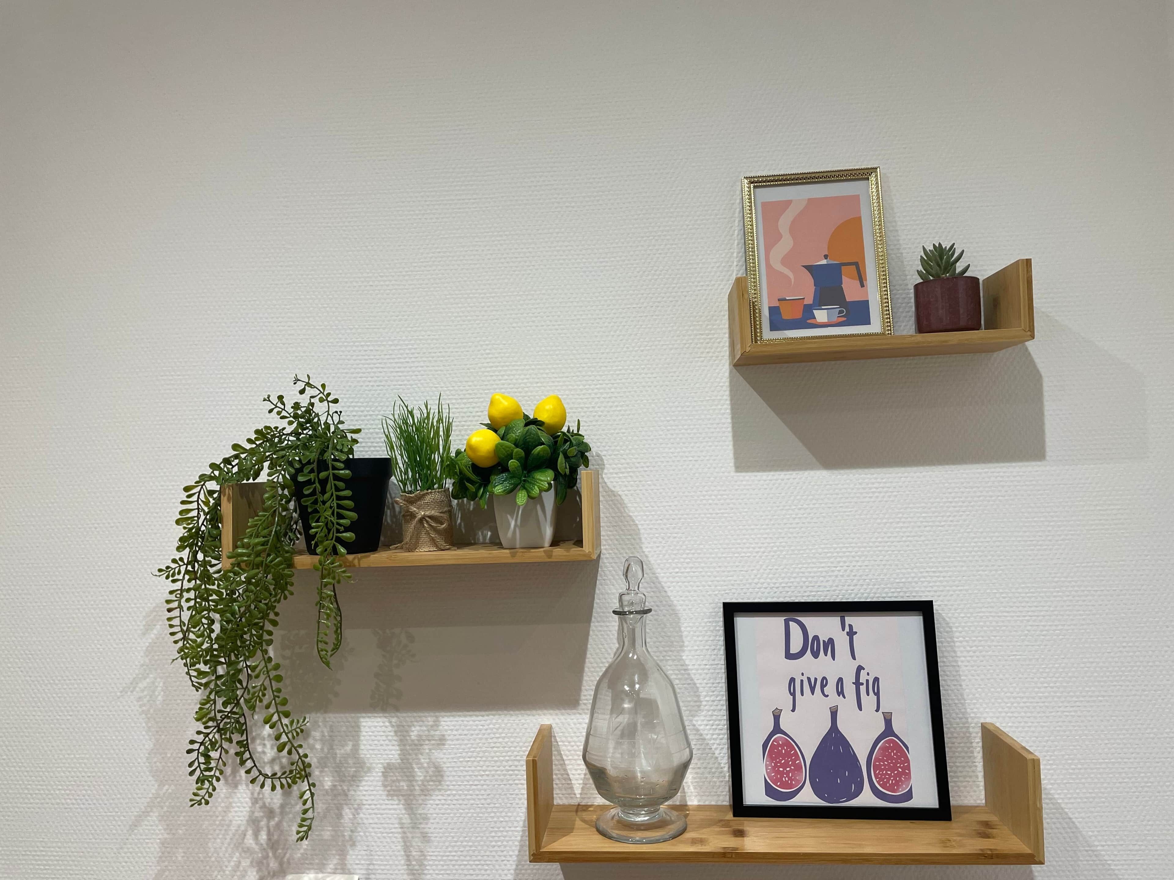 Two wooden shelves against a white wall, each holding plants, a framed picture, and a glass bottle.