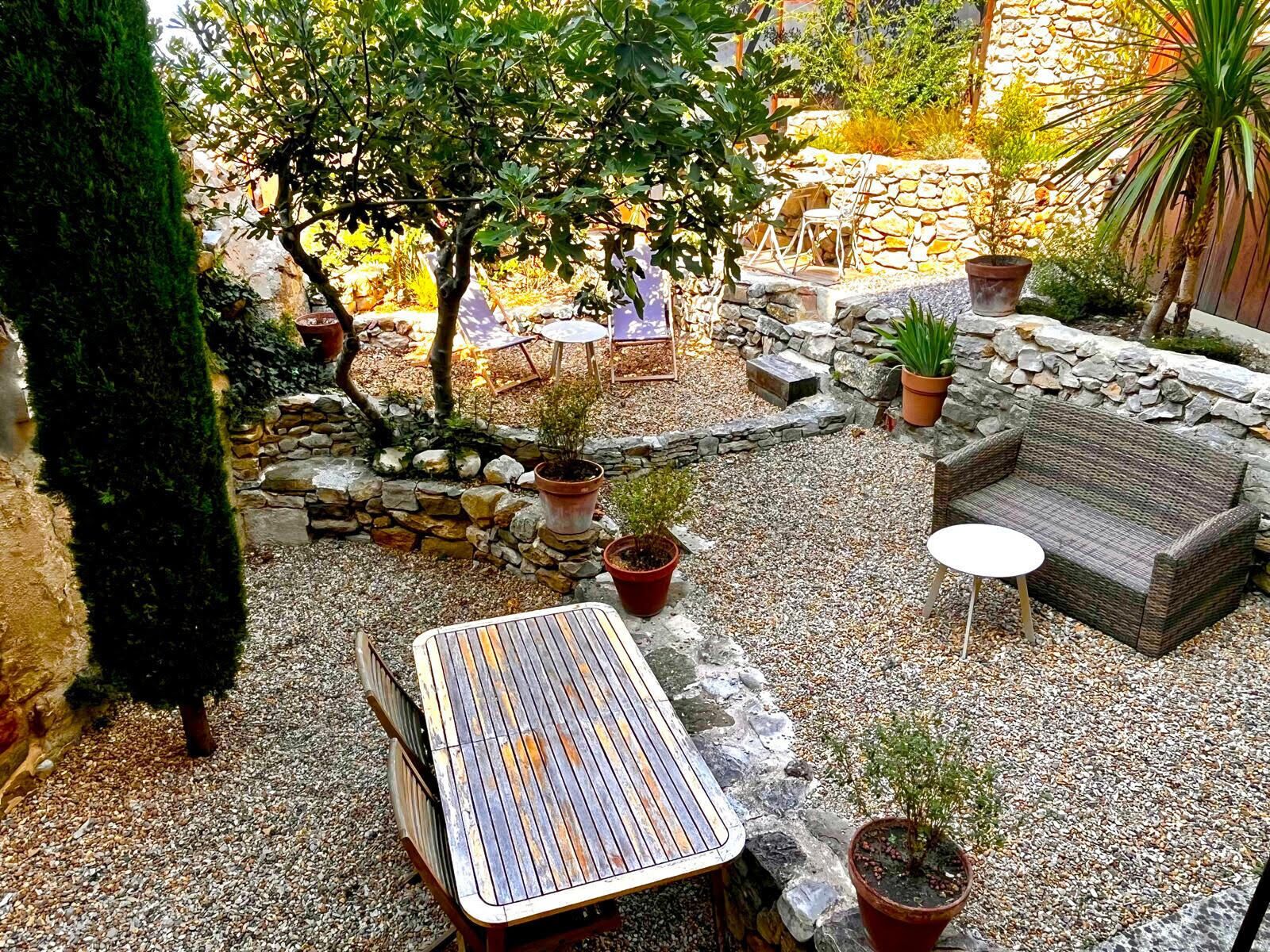 A patio area with a wooden table, a wicker sofa, and potted plants.
