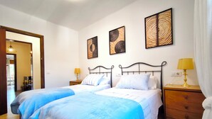 Een tweepersoonsbed met een blauwe spreidek, twee nachtkastjes met lampen, en drie kunstwerken aan de muur.
