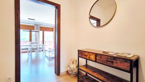 Een kamer met een houten console, een spiegel en uitzicht op een balkon met witte stoelen.