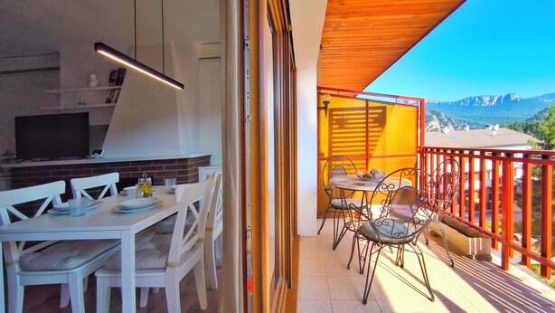 Een balkon met een eethoek, een televisie en uitzicht op bergen.