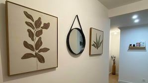 Un couloir orné de tableaux encadrés, avec un miroir rond et une petite étagère sur laquelle sont disposés des objets décoratifs.