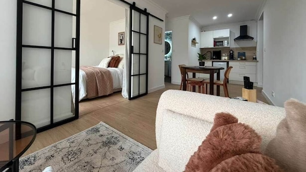 Un salon moderne avec un canapé, une cloison en verre, un coin repas et une cuisine en arrière-plan.