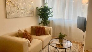 Un salon avec un canapé, une table basse, une plante, un tableau et un téléviseur.