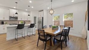 Una cocina moderna con armarios blancos, una isla central, taburetes de bar, una mesa de comedor con sillas e iluminación colgante.