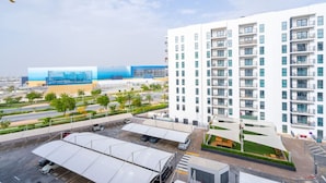 Un moderno edificio de gran altura con varios balcones, una zona de estacionamiento y un jardín ajardinado.