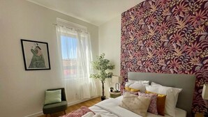 Une chambre à coucher avec un lit, une chaise, une plante et une fenêtre avec des rideaux.