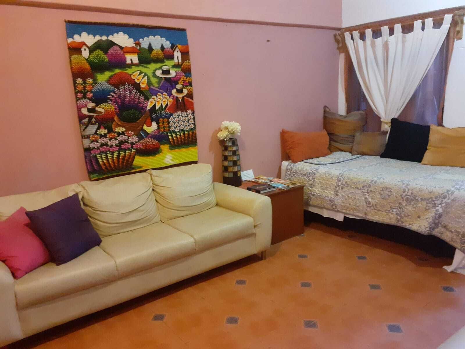 A room with a sofa, a bed, a painting, and a vase with flowers.