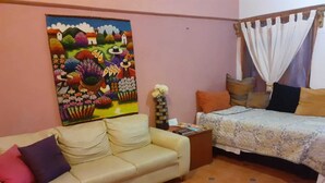Una habitación con sofá, cama, un cuadro y un florero con flores.
