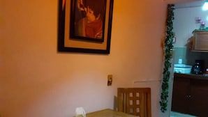 Una mesa de comedor con mantel blanco, un cuadro en la pared y una cocina visible al fondo.