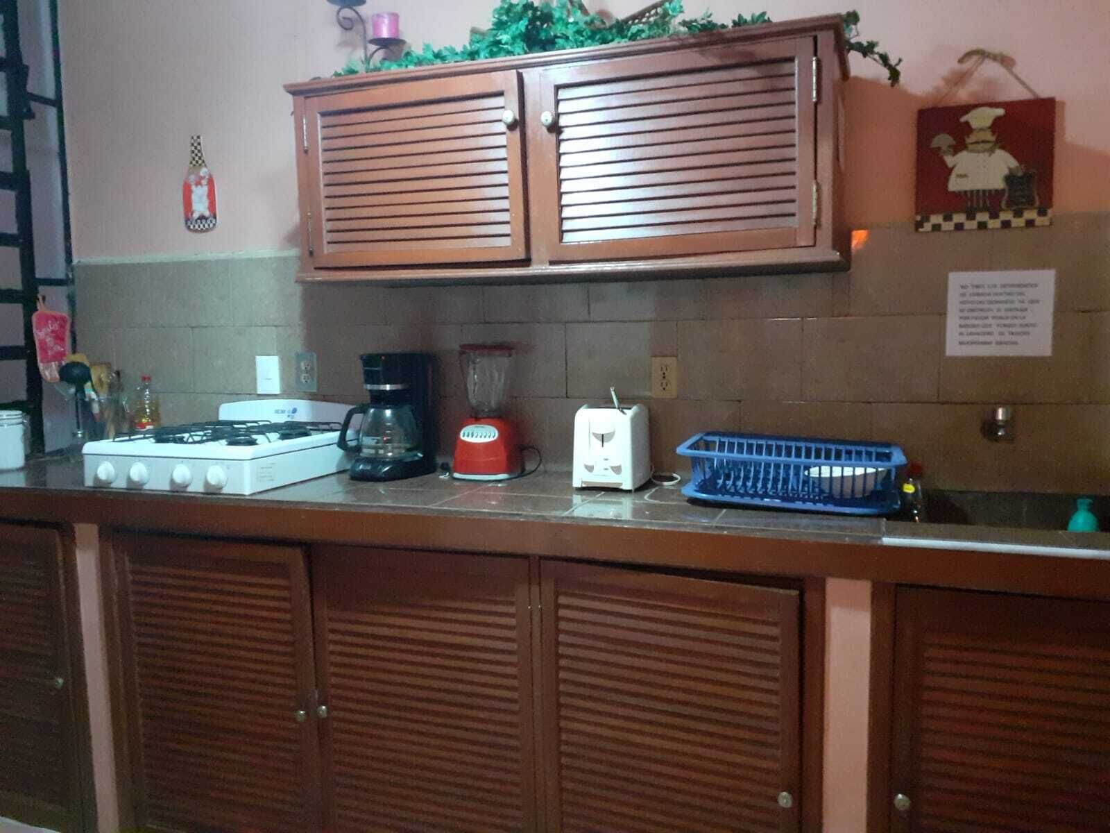 Una cocina con estufa a gas, cafetera, licuadora, tostadora y un escurreplatos azul.
