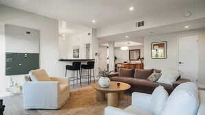Una sala de estar moderna con un sofá, sillones, una mesa de centro y una cocina al fondo.