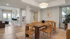 Un comedor amplio con una mesa y sillas de madera, un colgante de luz y vistas a la cocina al fondo.